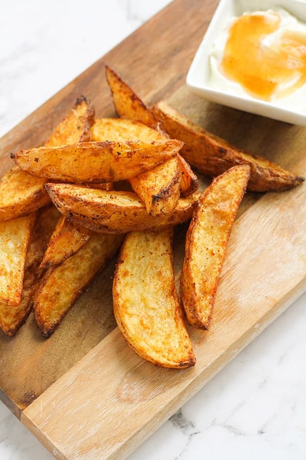 potato wedges and dipping sauce on a wooden cutting board.