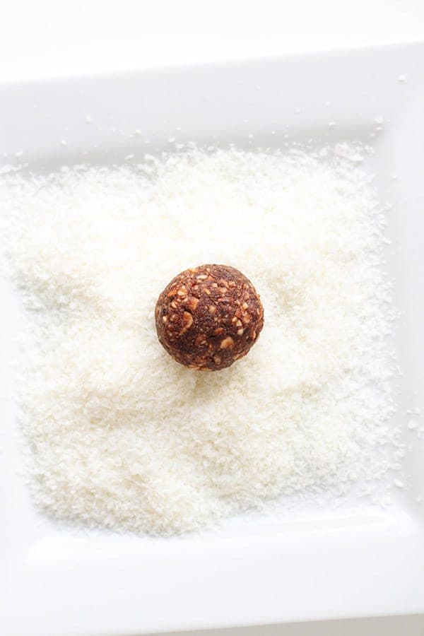 shredded coconut on a white plate with an energy ball on top.