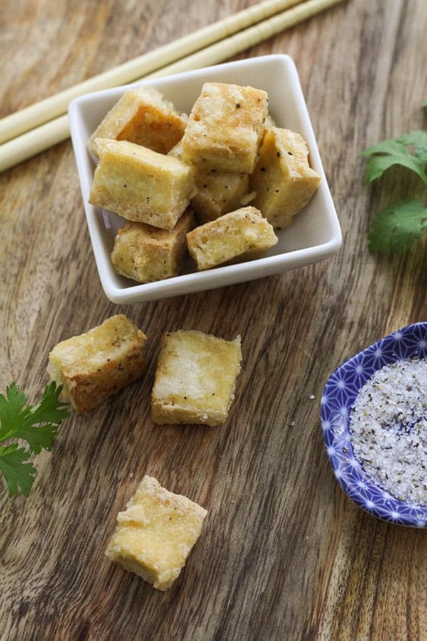 pieces of salt and pepper tofu scattered on a wooden board.