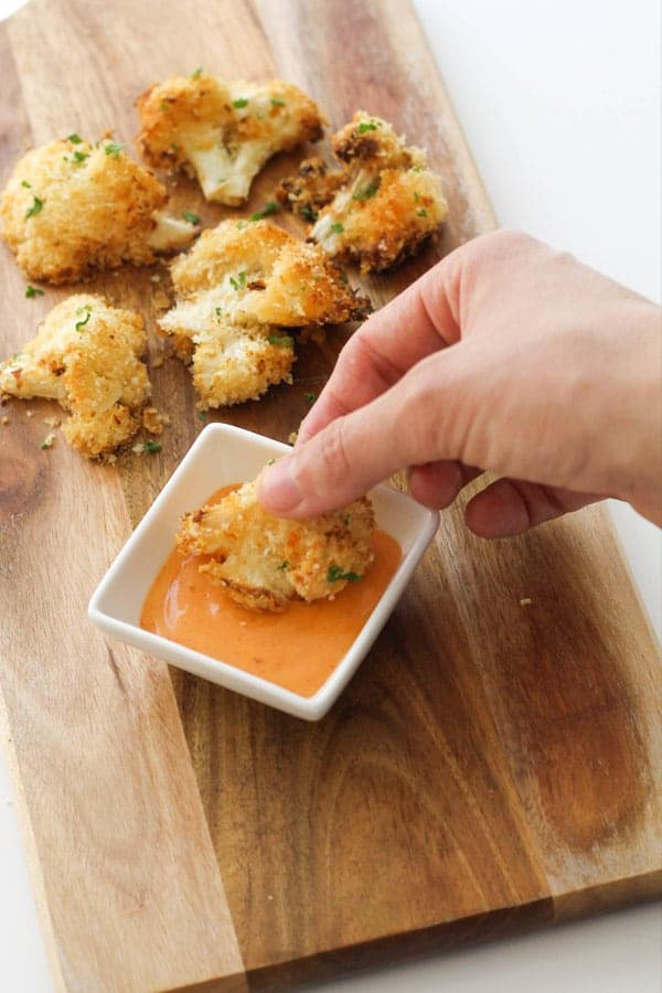 hand dipping a piece of bang bang cauliflower into sauce.