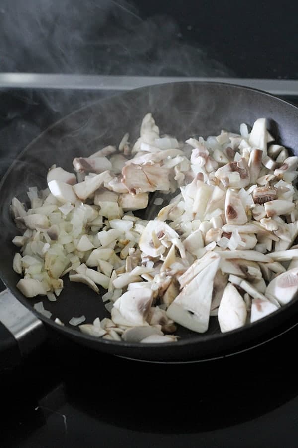 onion and mushroom being sautéed in a frying pan.