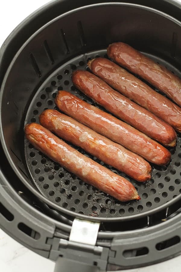 cooked sausages in air fryer basket.