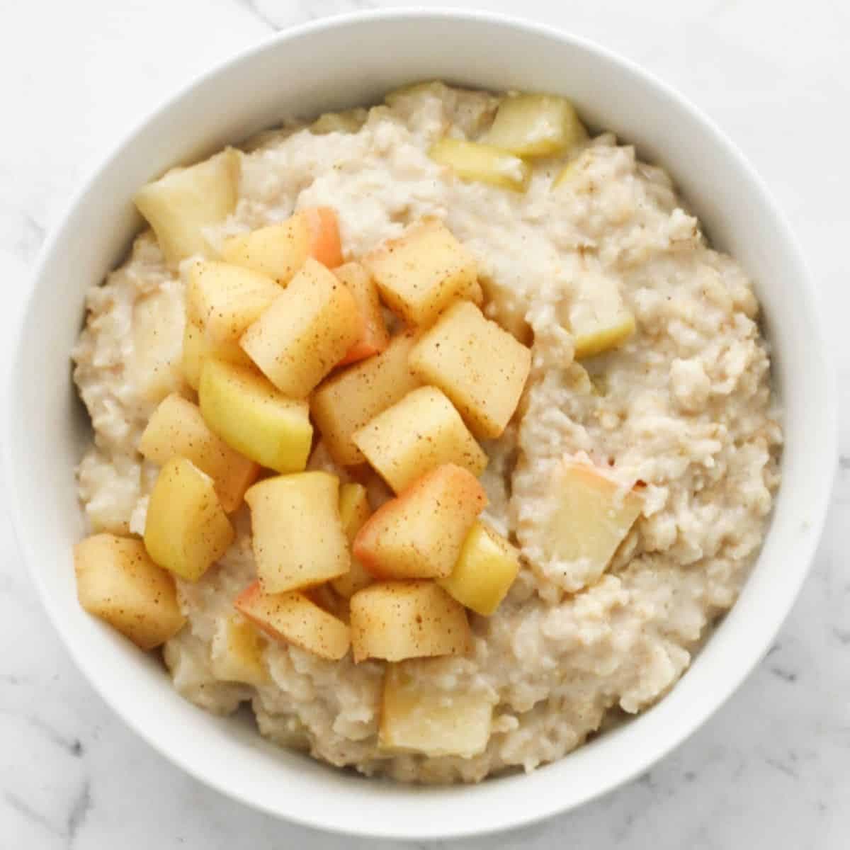 apple cinnamon oatmeal in a white bowl topped with stewed apples.