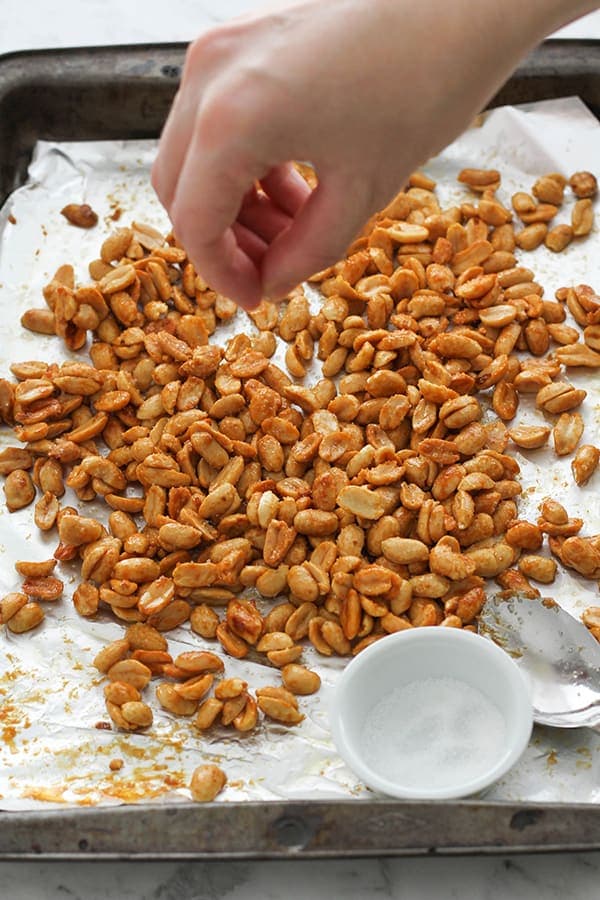 roasted peanuts on a baking tray with a hand sprinkling sugar on top.