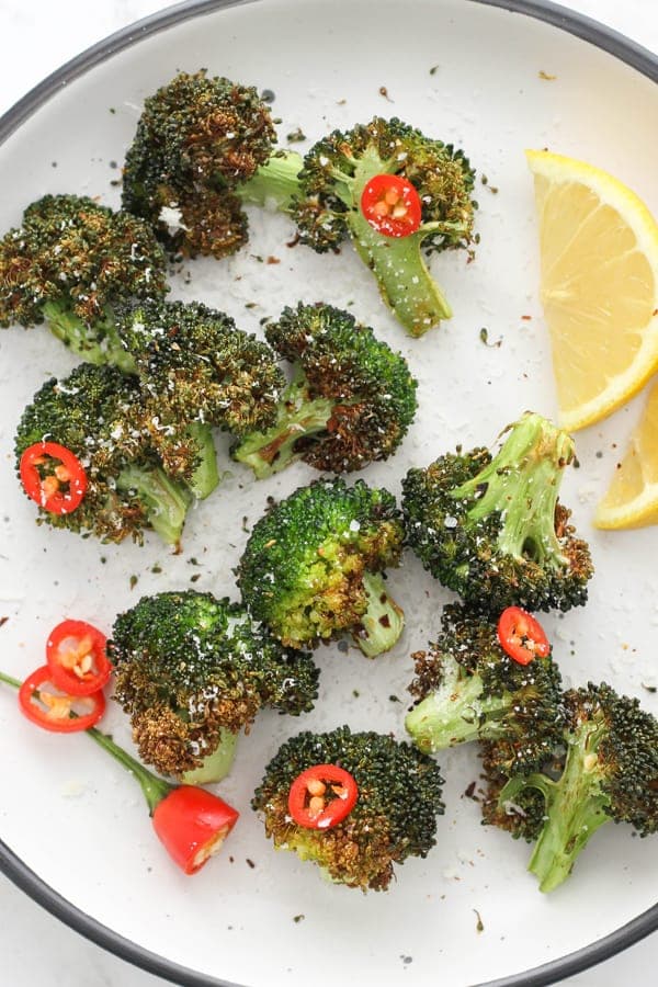 roasted broccoli on a white plate with lemon wedges and chopped chilli.