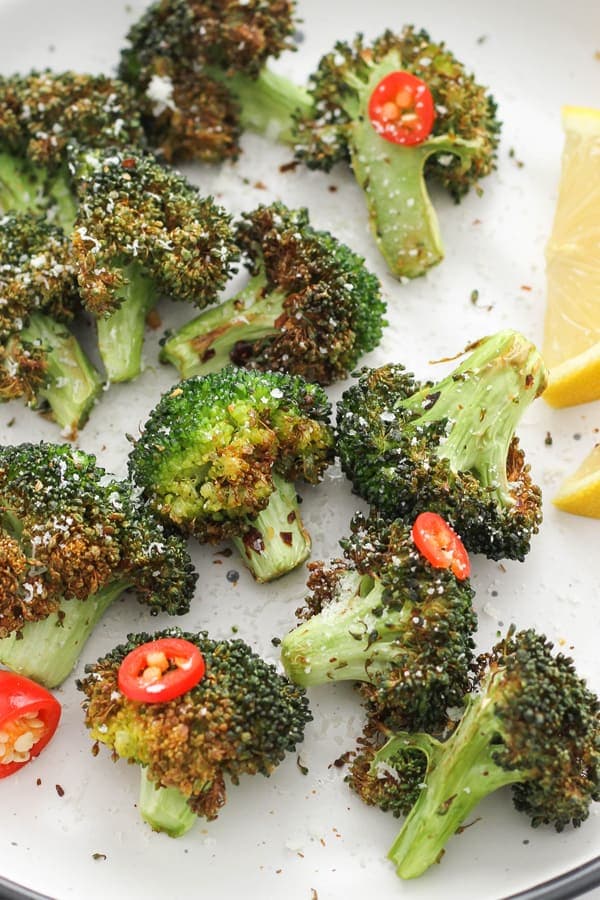 roasted broccoli on a white plate with lemon wedges and chopped chilli.