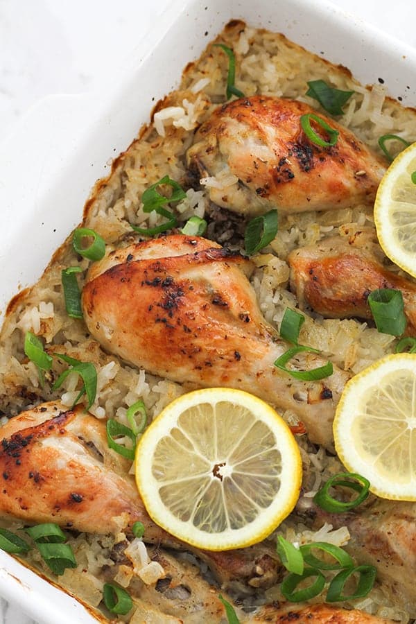 chicken drumsticks on top of a bed of rice in a baking dish, topped with lemon slices.
