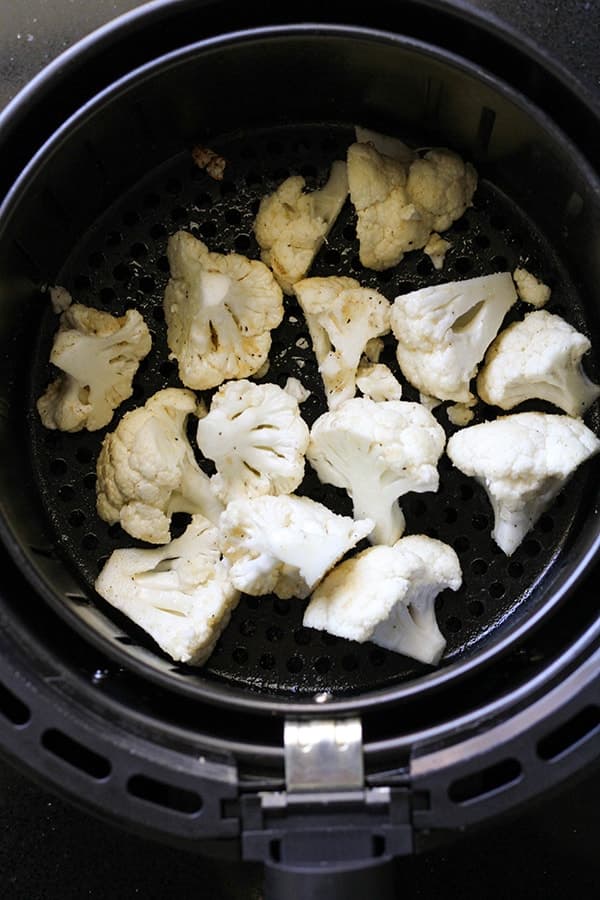 cauliflower florets in an air fryer basket.