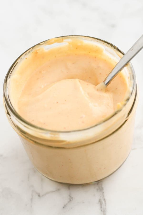 sriracha aioli in a glass jar with a spoon stuck inside.