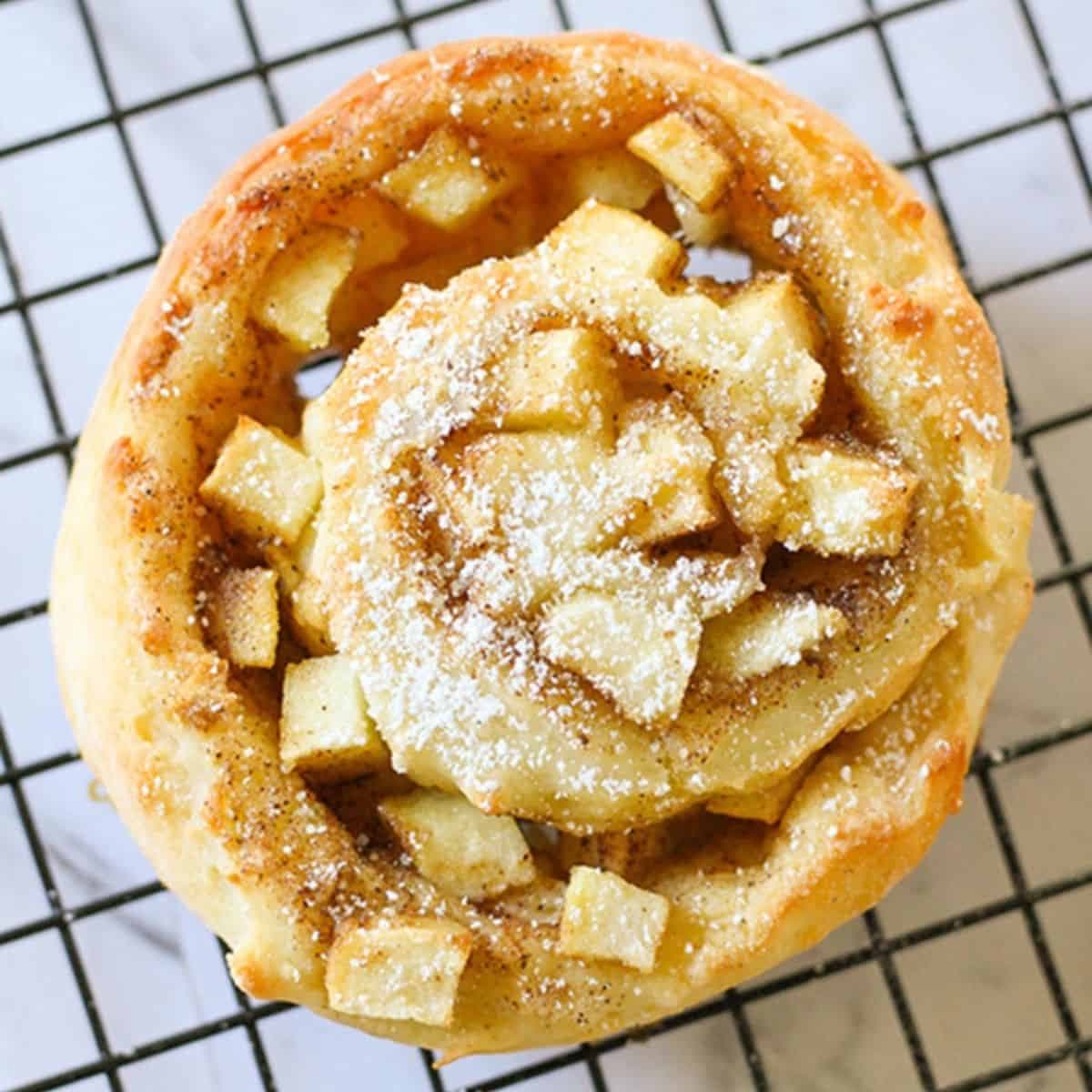 an apple cinnamon roll sitting on a wire rack.