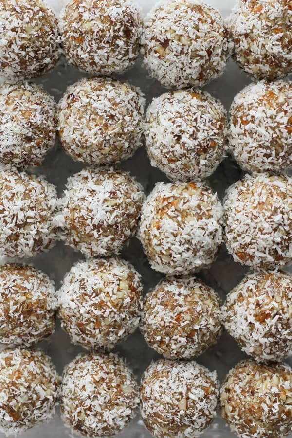 coconut date balls lined up together in a glass container.