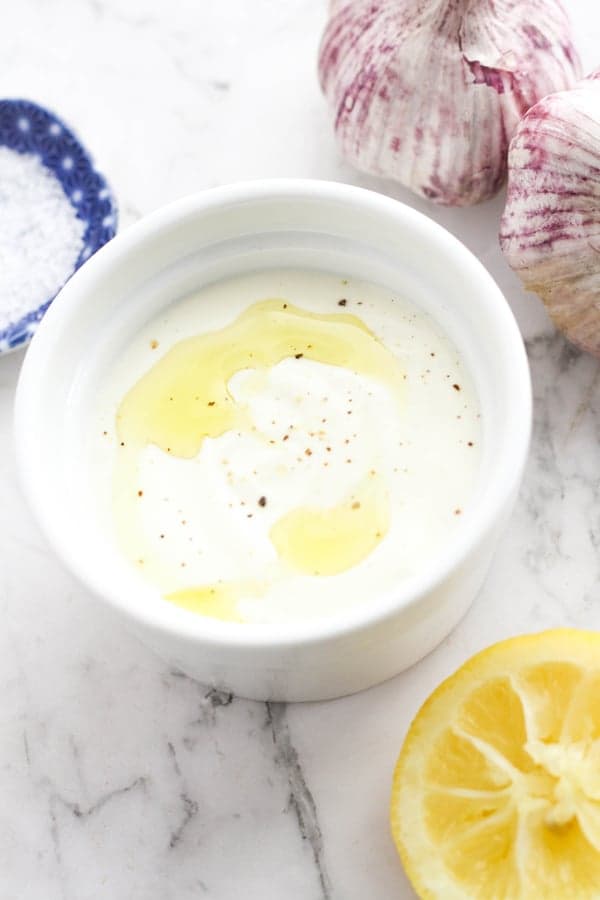 sauce in a white bowl surrounded by lemon, garlic and salt.