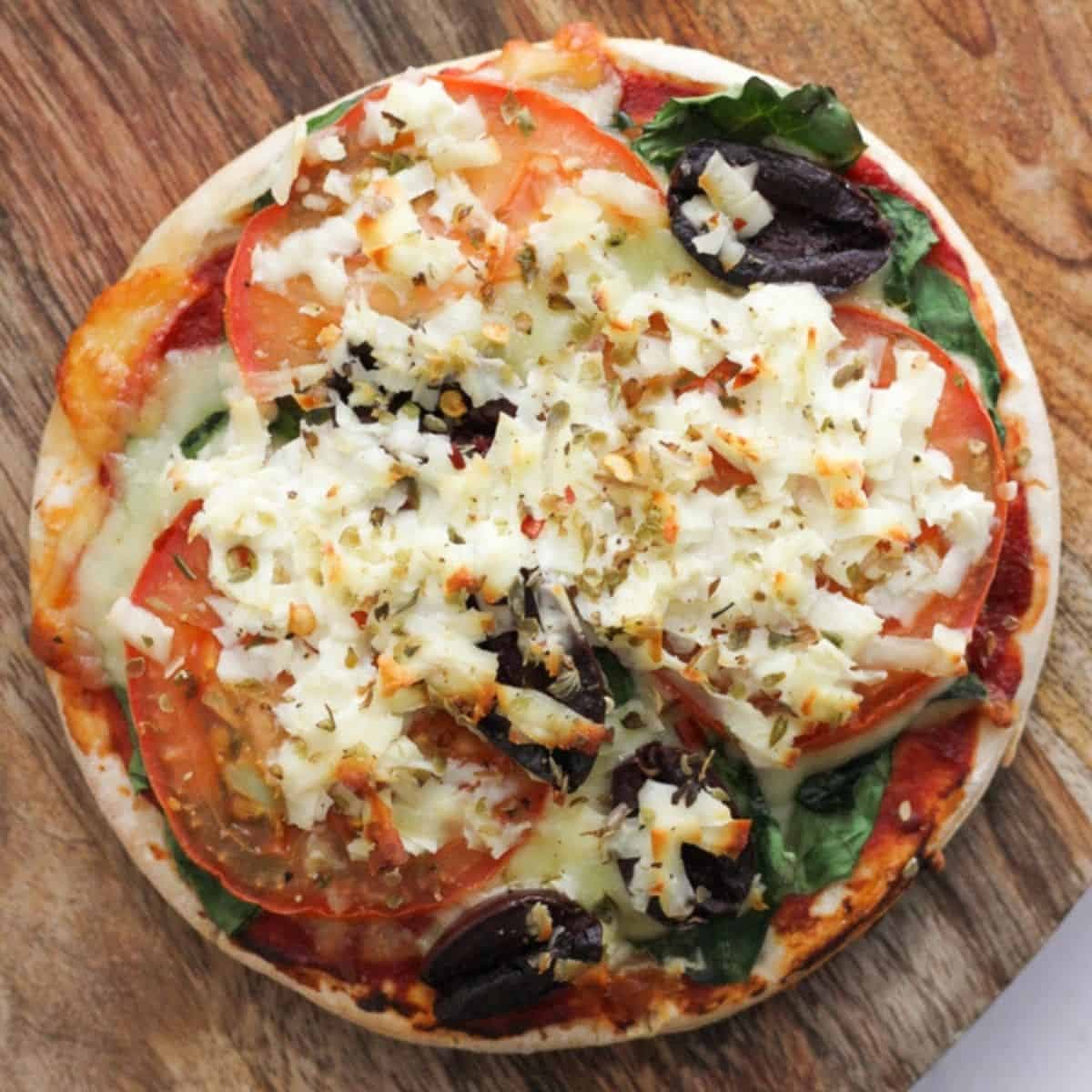 pizza topped with halloumi, spinach and tomato on a wooden serving board.