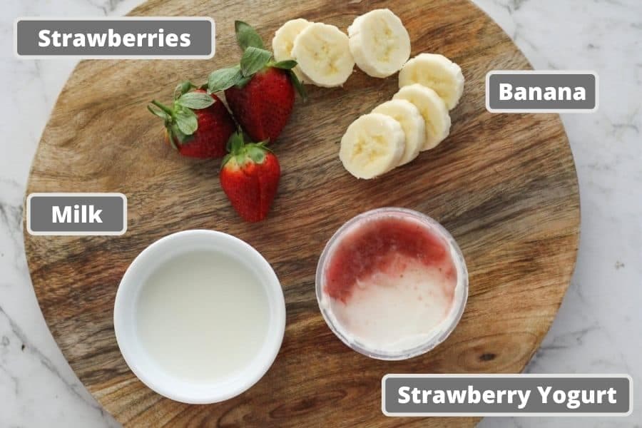 ingredients for strawberry smoothie including milk, yogurt, banana slices and strawberries.