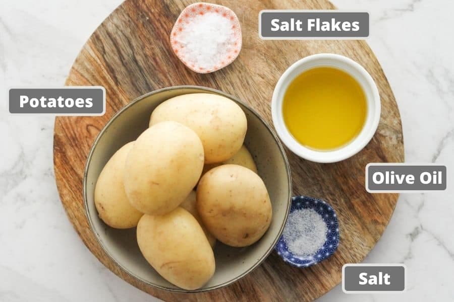 ingredients for glass potatoes on a wooden board including olive oil and salt flakes.
