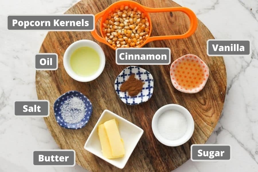 ingredients for cinnamon sugar on a wooden board including popcorn kernels, butter and sugar.