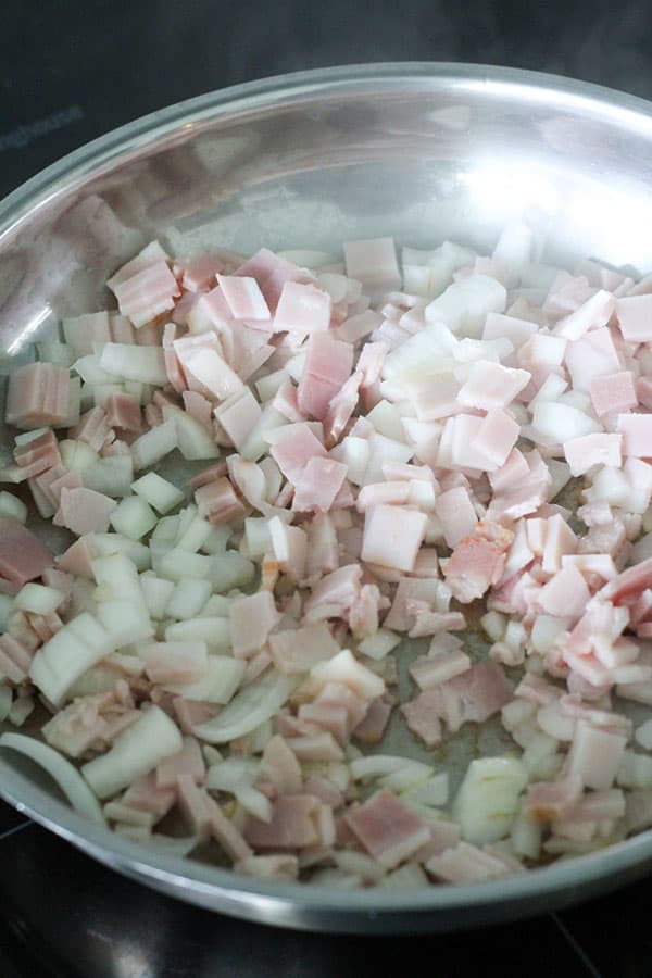 bacon and onion being fried in a frying pan.