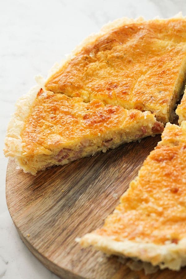 bacon and egg pie sliced on a wooden board with a piece missing.