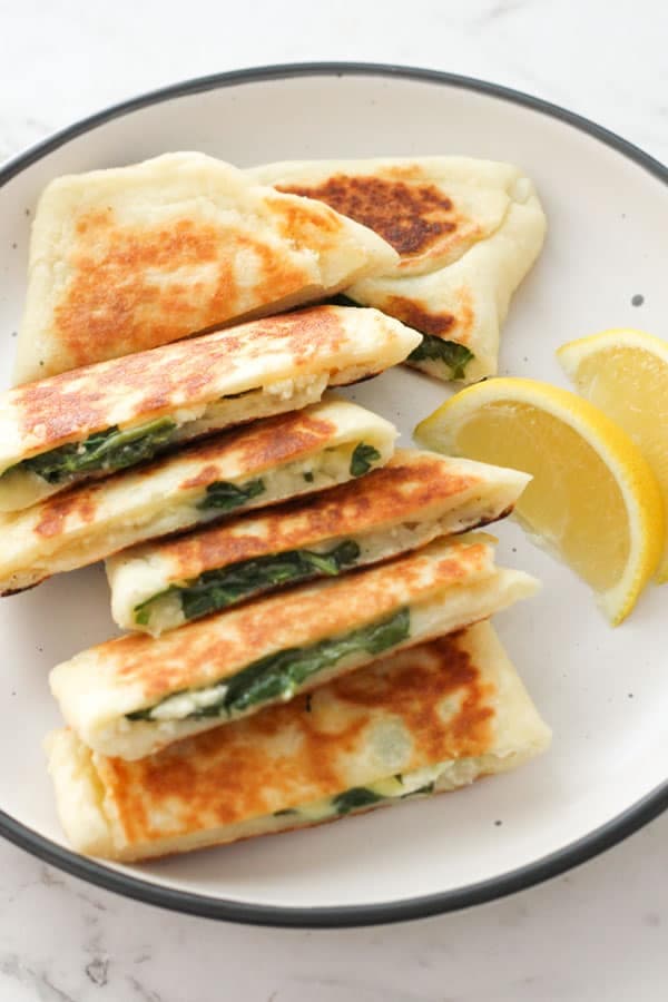 spinach and feta gozleme stacked on top of each other on a white plate.