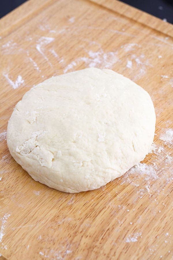 scone dough in a large disc shape on a wooden board.