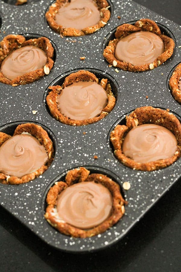 caramel tarts topped with chocolate in a muffin tray.
