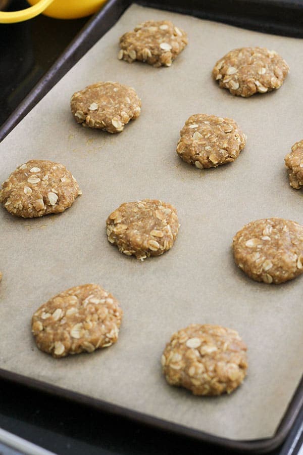 uncooked anzac biscuits on a baking tray.