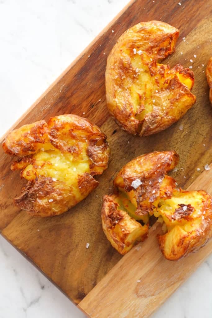 three crispy smashed potatoes on a wooden board.