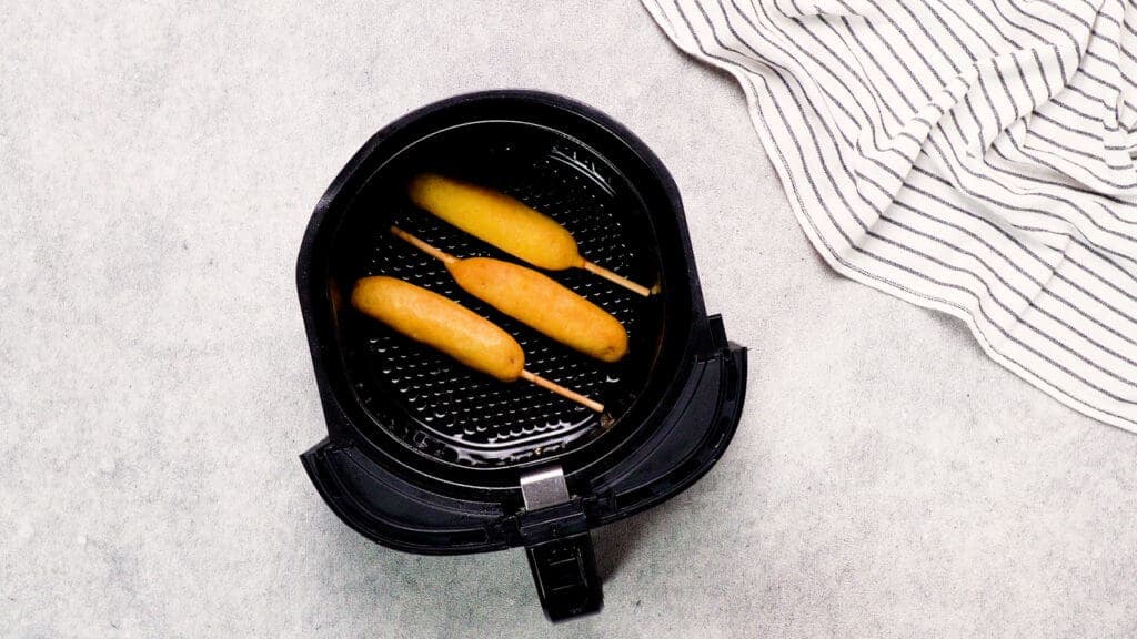 top shot of air fryer basket with prepared frozen corn dogs in it