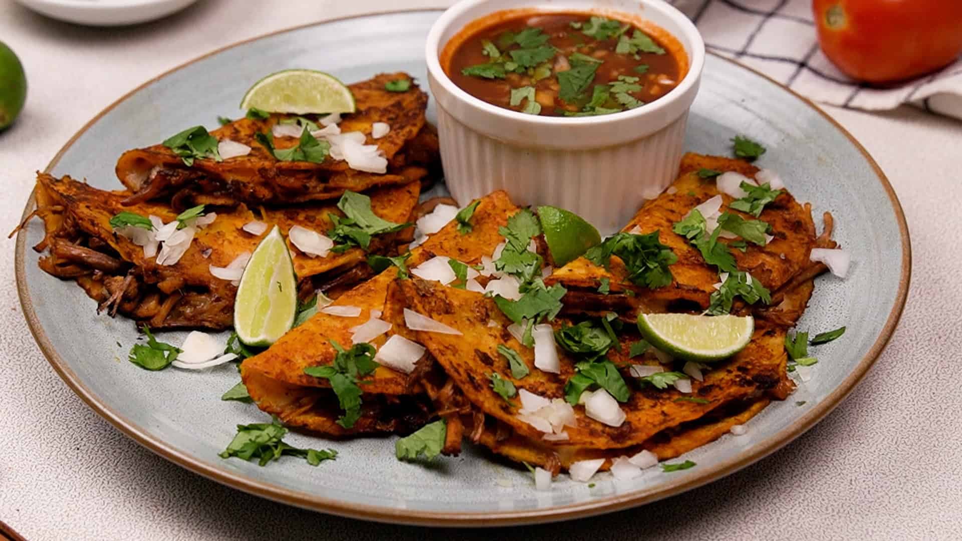 Serve with diced onion, cilantro, lime wedges, and the remaining consommé as a dipping sauce. Enjoy!
