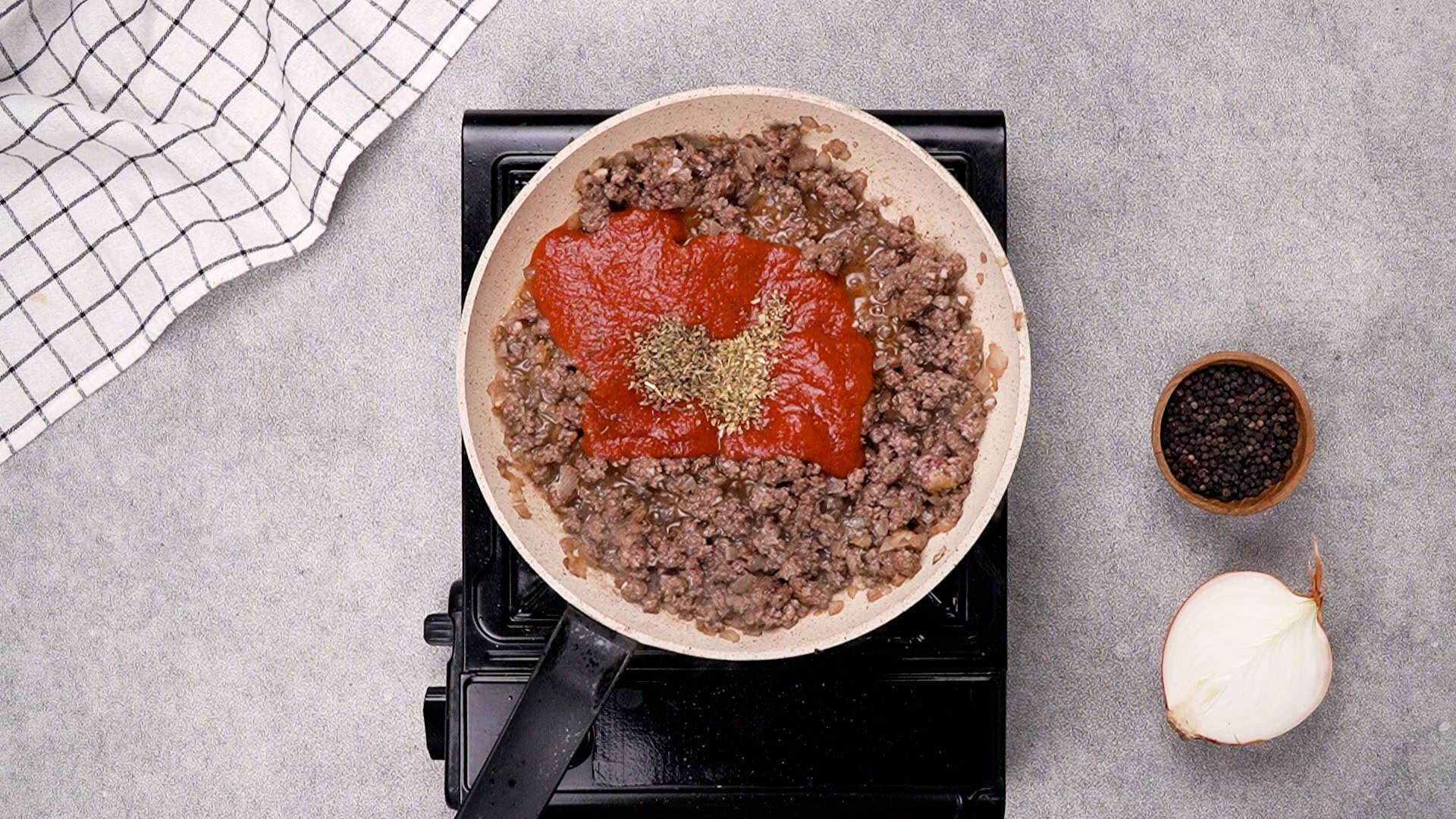 Once the beef is browned, stir in the pizza sauce, dried oregano, and dried basil. Cook the mixture for 4 minutes to combine the flavours.