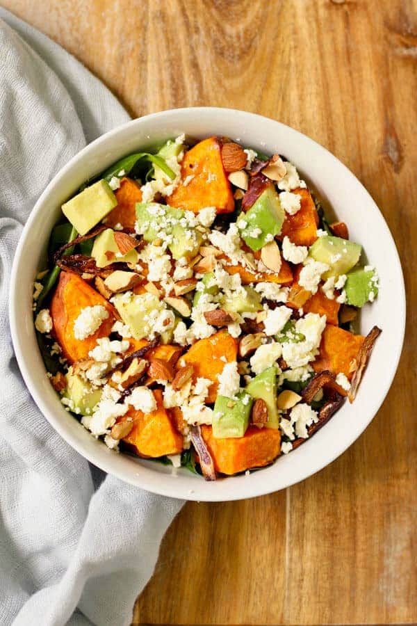sweet potato, avocado and feta salad in a white bowl on a wooden cutting board
