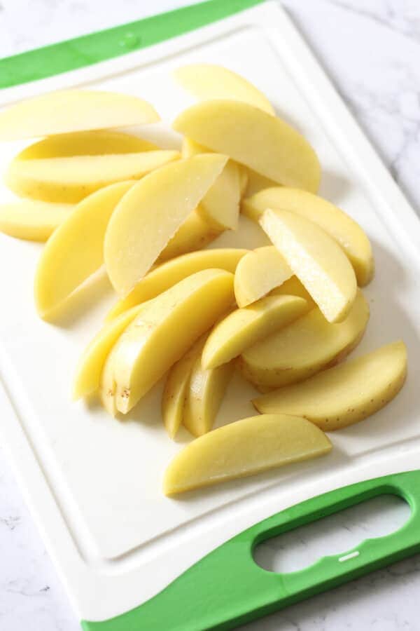 potatoes cut into thin wedges on a cutting board.