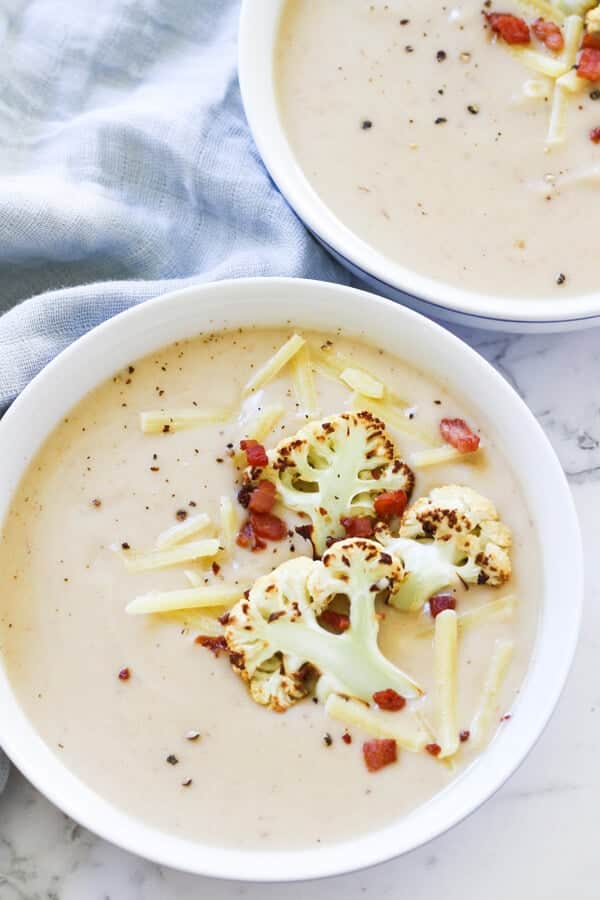 cauliflower and bacon soup in a white bowl topped with bacon bits and roasted cauliflower pieces