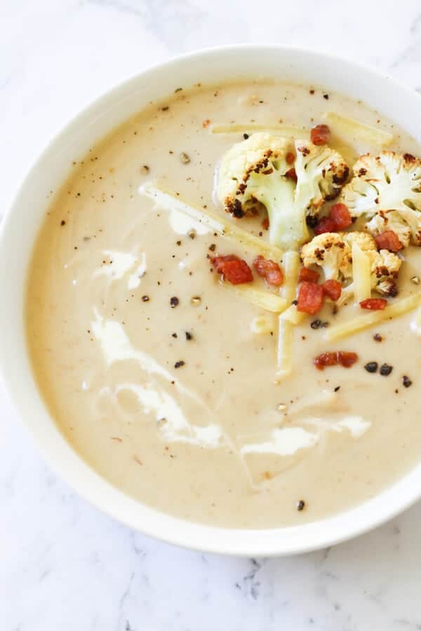 cauliflower and bacon soup in a white bowl topped with bacon bits and roasted cauliflower pieces