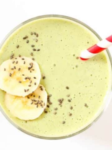 green smoothie in a glass topped with chia seeds and banana slices
