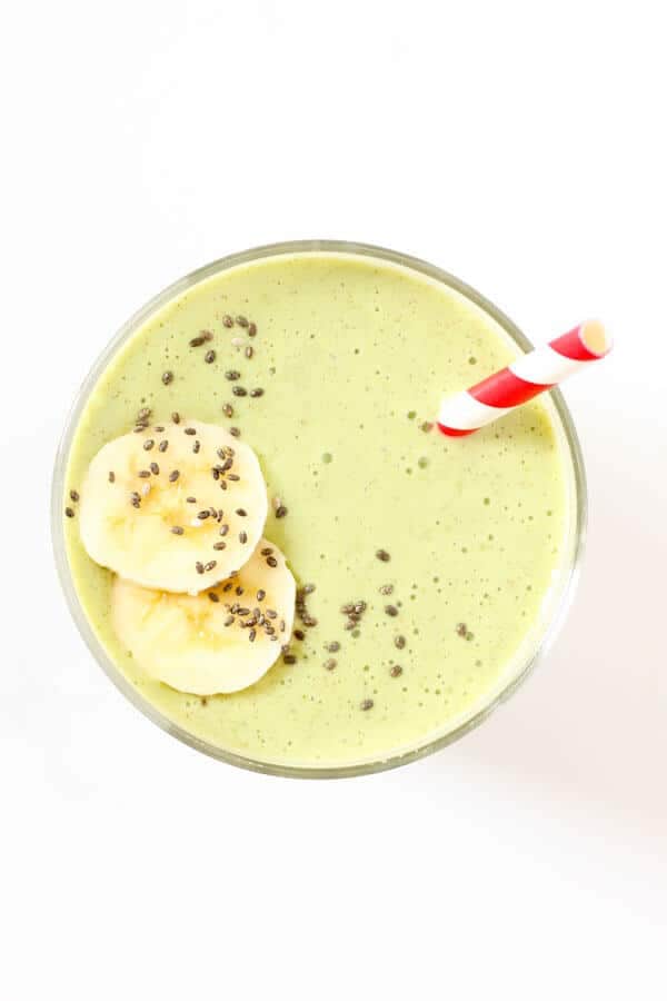 spinach mango smoothie in glass with red straw and banana slices on top