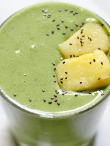 kale pineapple smoothie in a short glass topped with pineapple pieces and chia seeds