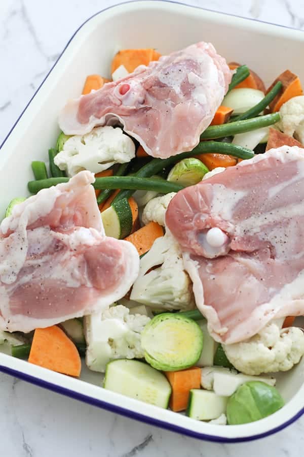 chicken thighs laying skin side down on a tray of vegetables