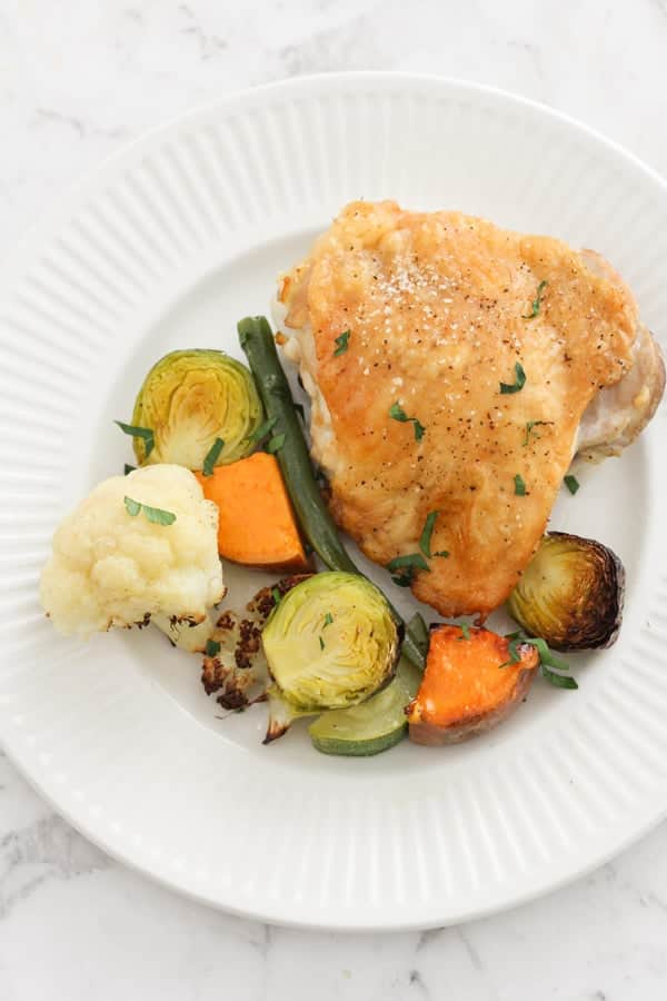 crispy baked chicken thigh and vegetables on a white plate.