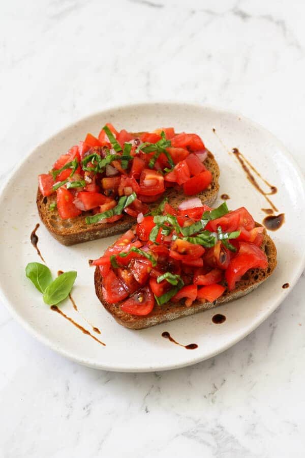 two pieces of bruschetta on a white plate covered in balsamic glaze.