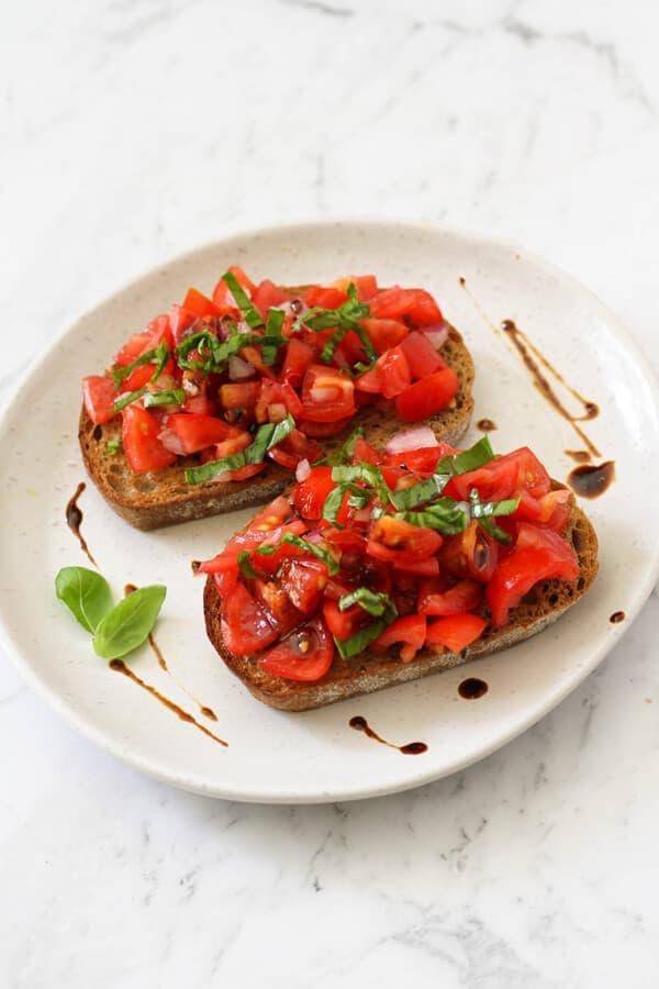 two pieces of bruschetta on a white plate covered in balsamic glaze.