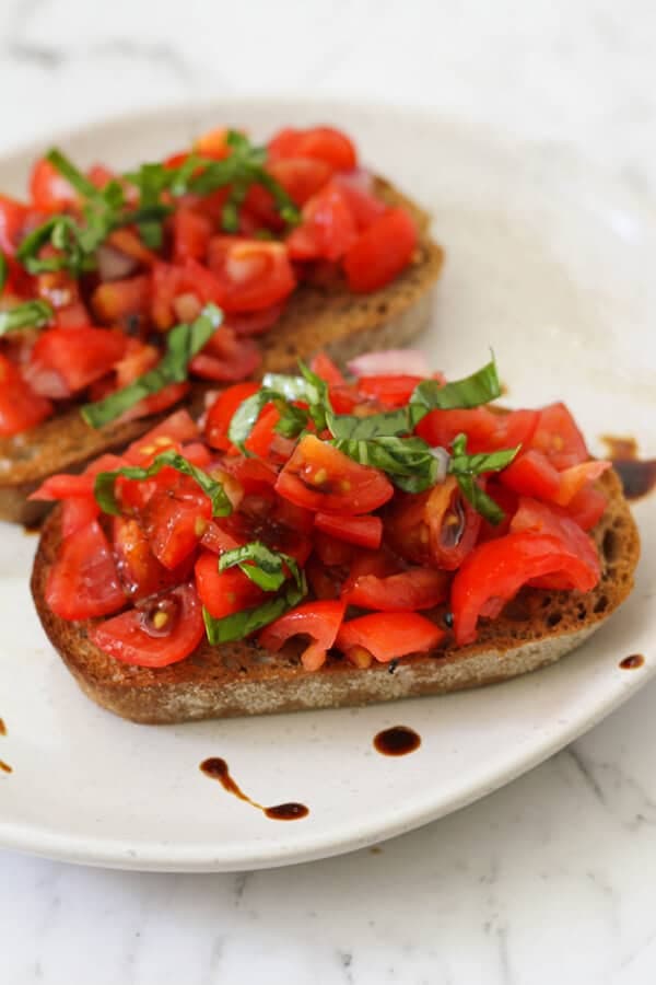 two pieces of bruschetta on a white plate covered in balsamic glaze.