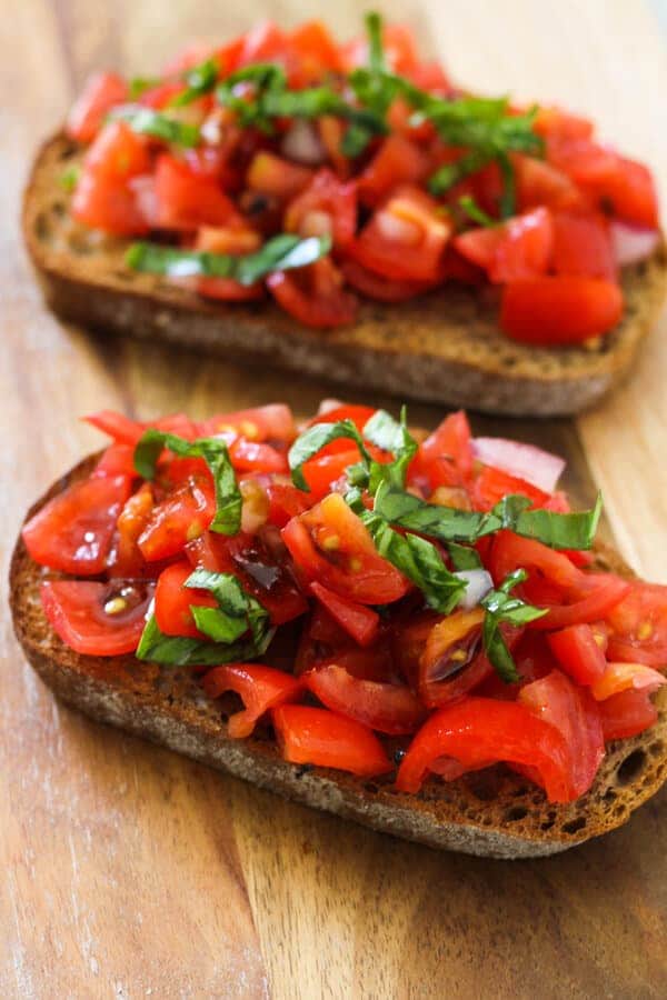 two pieces of bruschetta on a wooden board covered in balsamic glaze.