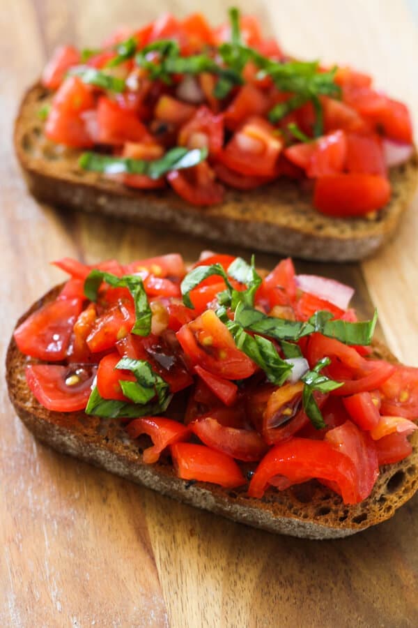 two pieces of bruschetta on a wooden board covered in balsamic glaze.