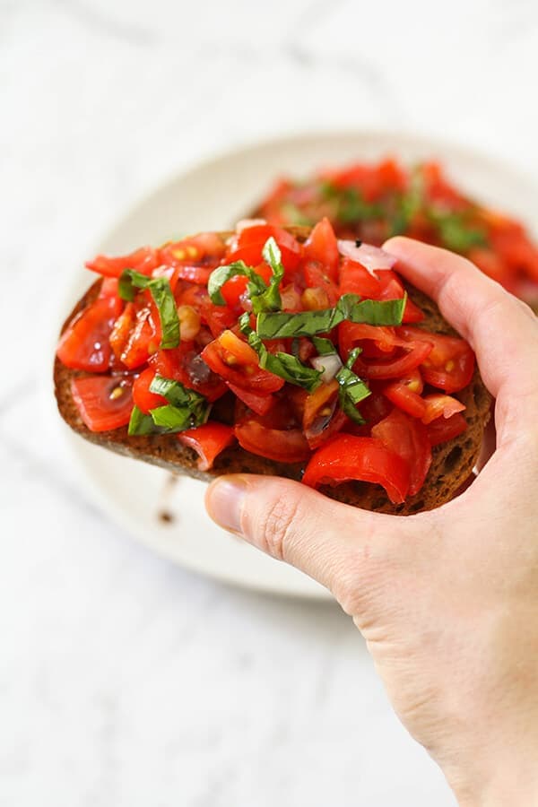 a hand holding a piece of bruschetta.