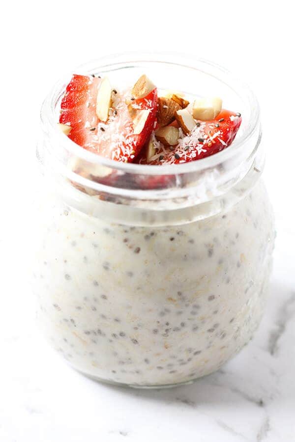 jar of overnight oats topped with strawberries, shredded coconut and almonds.