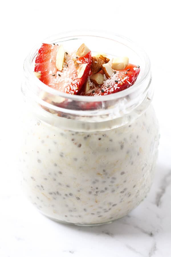 jar of overnight oats topped with strawberries, shredded coconut and almonds.