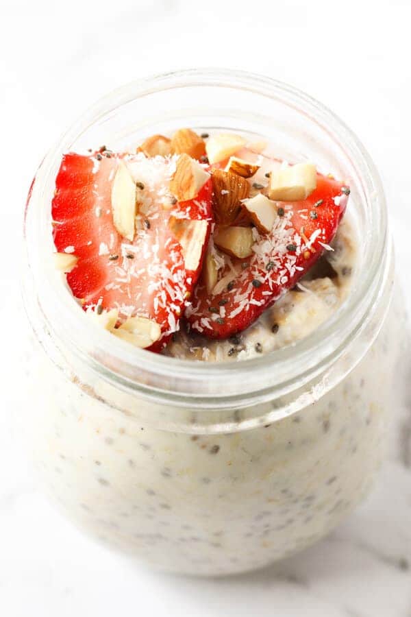 jar of overnight oats topped with strawberries, shredded coconut and almonds.