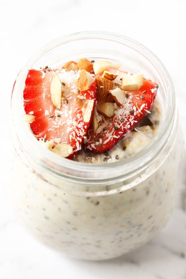 jar of overnight oats topped with strawberries, shredded coconut and almonds.