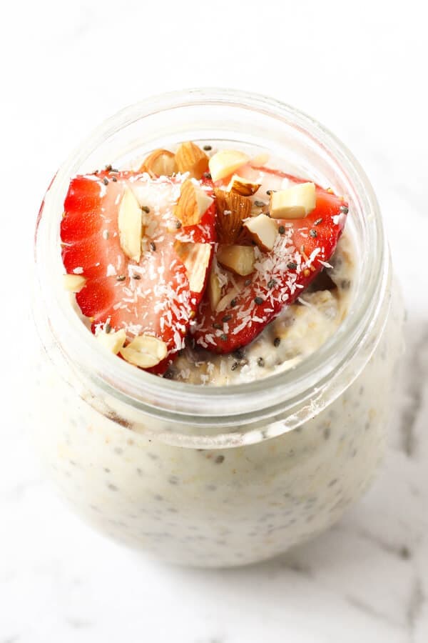 jar of overnight oats topped with strawberries, shredded coconut and almonds.